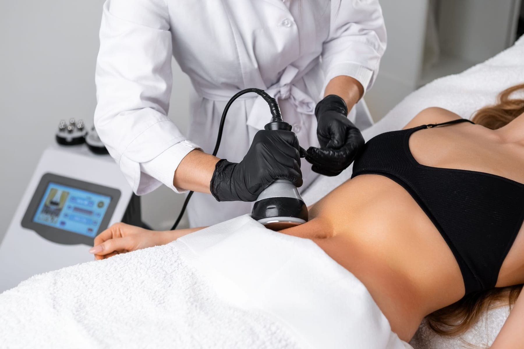 Body sculpting treatment device prepared on cream linen with a practitioner hand nearby.