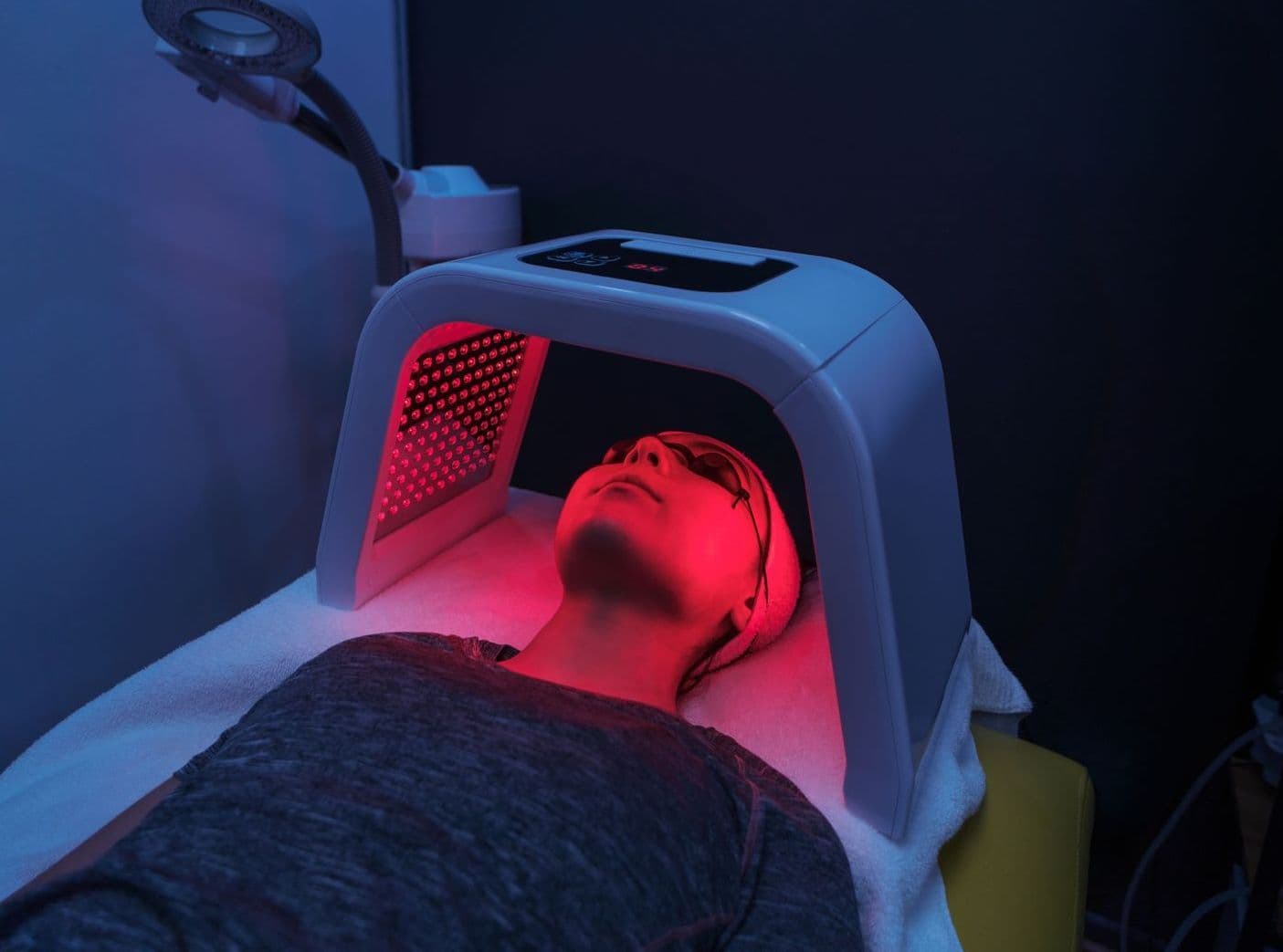 Empty red light therapy room with warm LED panel glowing above a cream treatment table.