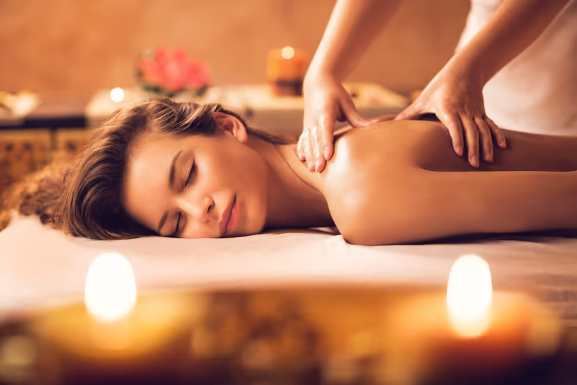 Massage therapist applying focused pressure through cream linen over a client shoulder.